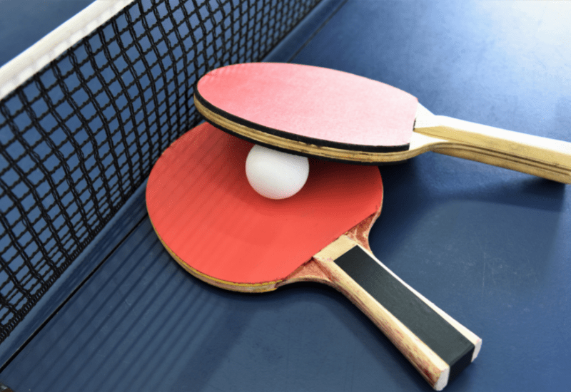 photo showing two table tennis racquets and a ball resting on a table tennis table