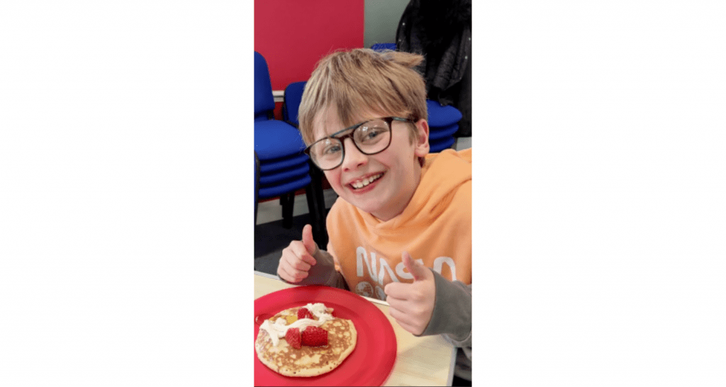 photo of young boy about to eat pancakes, indicating his approval with his thumbs up