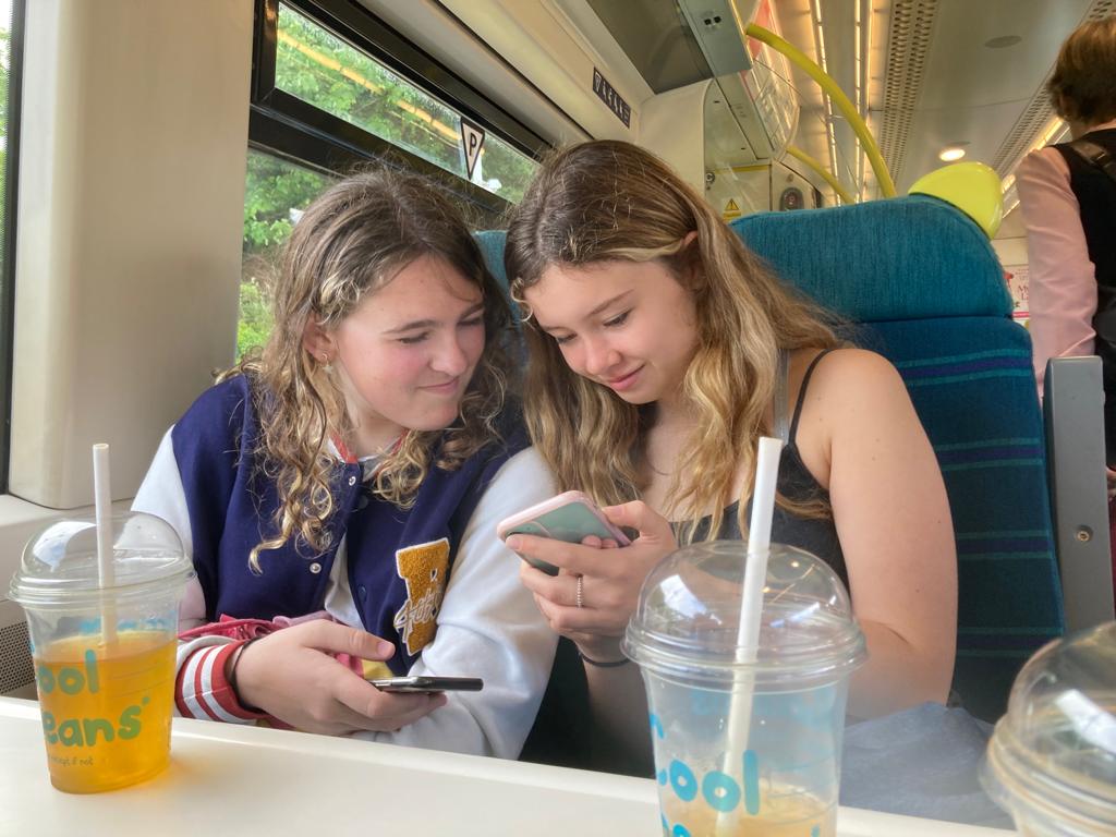 photo of Ella and friend sitting on a train and looking at a phone