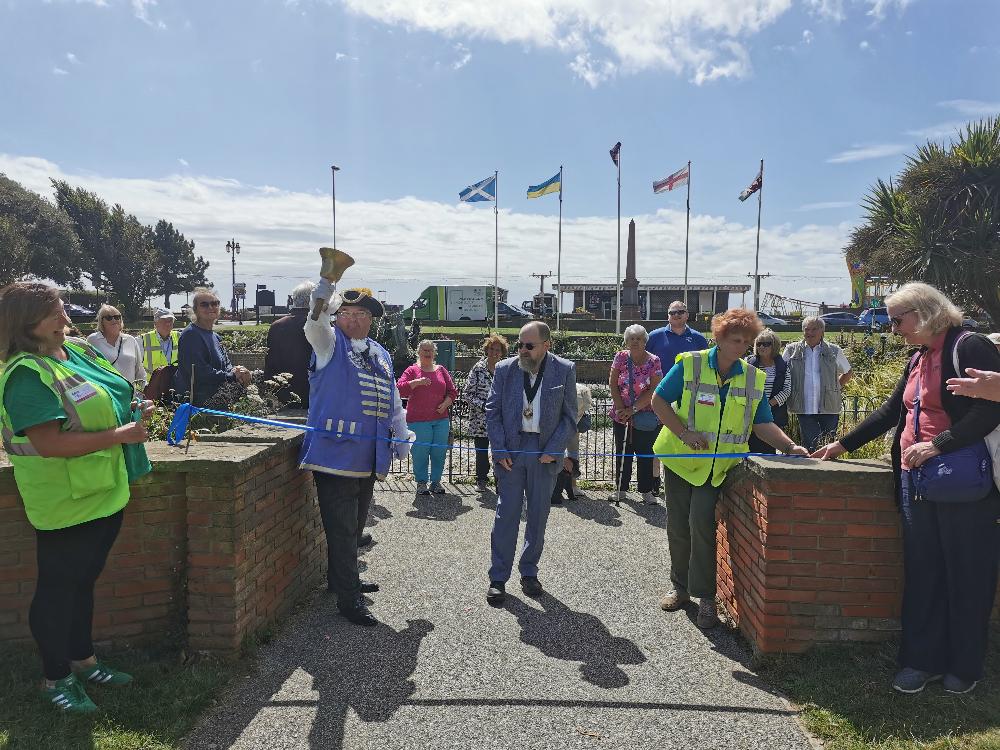 a photo of the official opening of the sensory garden on the Steyne in Worthing. Bob Smytherman, in his role as Town Crier, is featured, as is the mayor, members of the SSW staff and board, as well as SSW members. They look on as the blue ribbon is cut by the mayor.