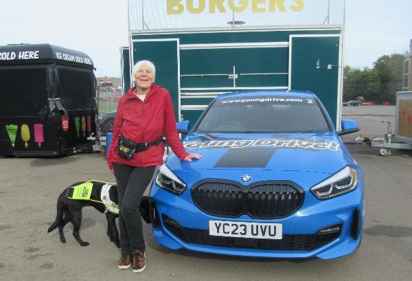 photo of a SSW member with their guide dog standing next to a racing car