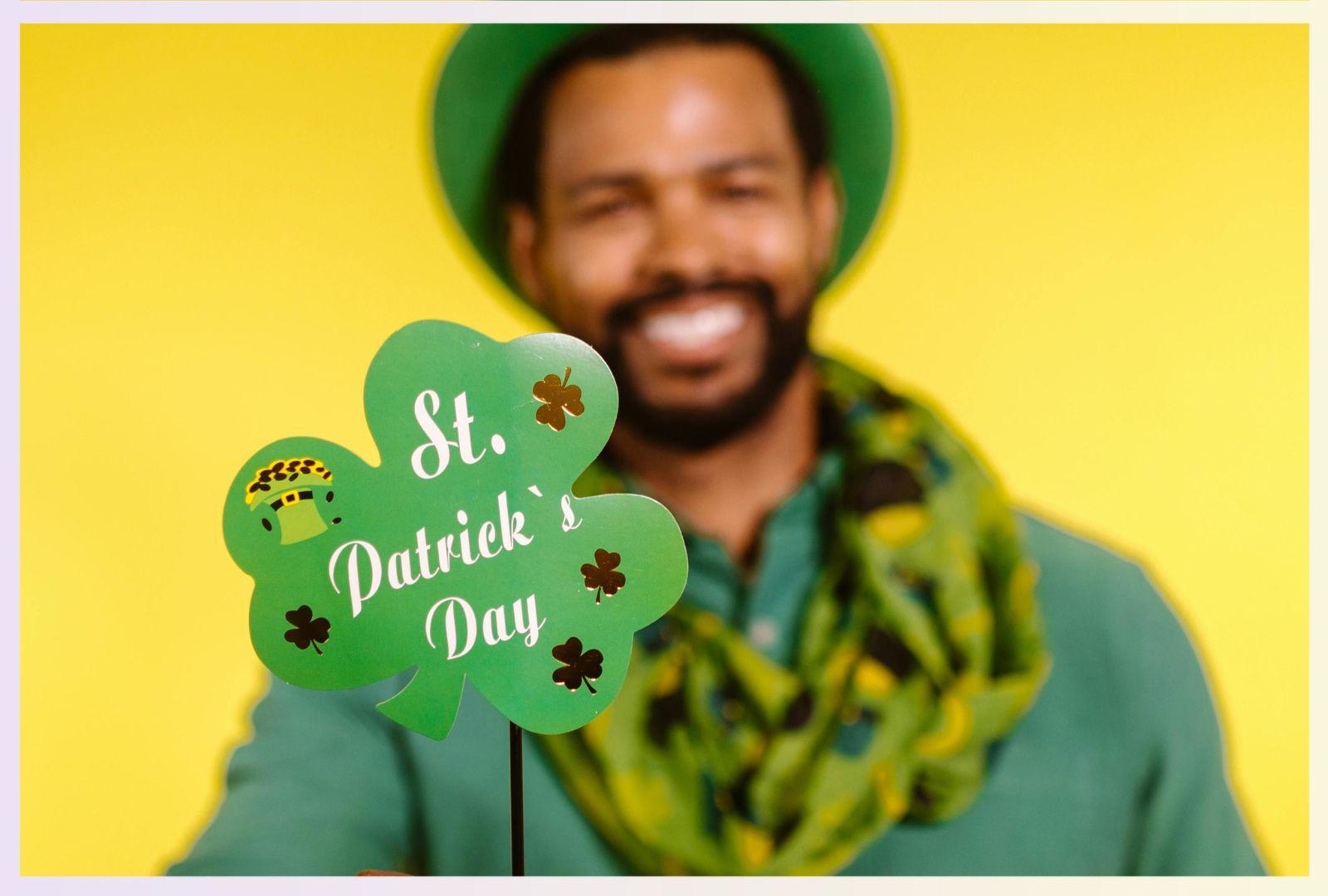 a man holding a clover shaped sign saying 'St Patricks Day'