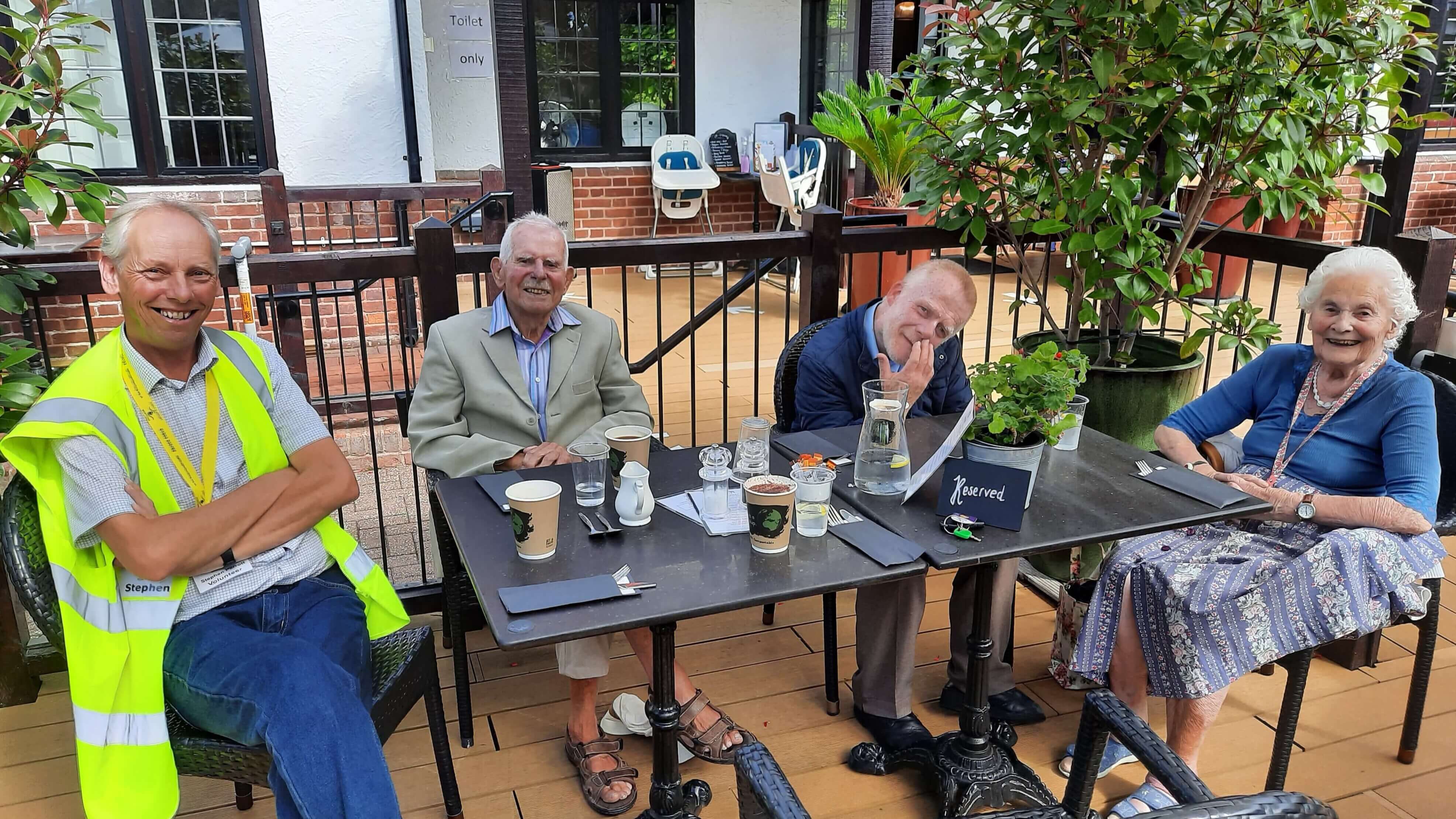 A volunteer and 3 members sitting at a table outside of a pub.