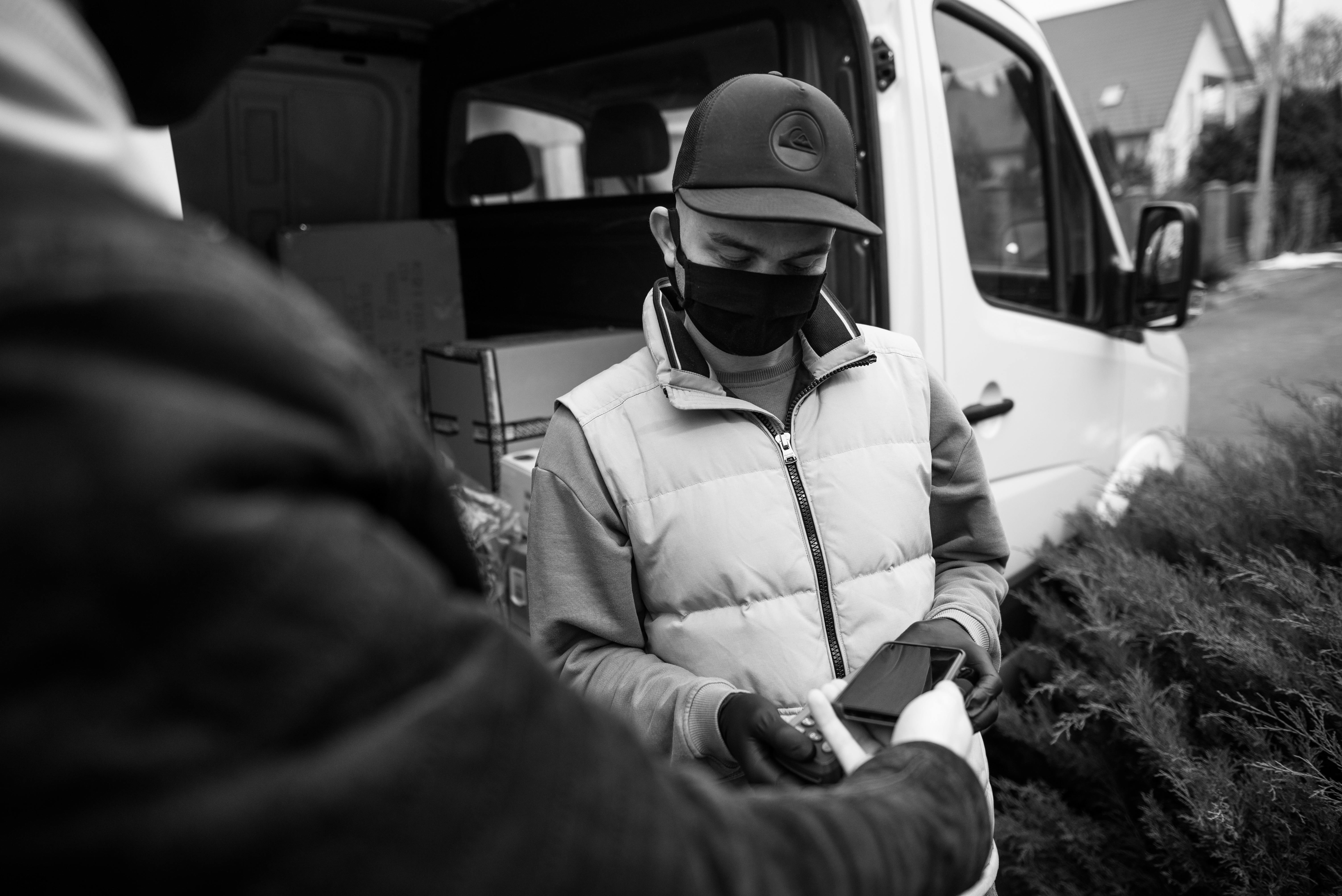 Black and white photo of a man wearing a face mask, taking a contactless payment.